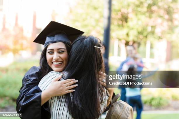 nach dem abschluss schließt die tochter die augen, während sie die mutter umarmt - graduation hat stock-fotos und bilder