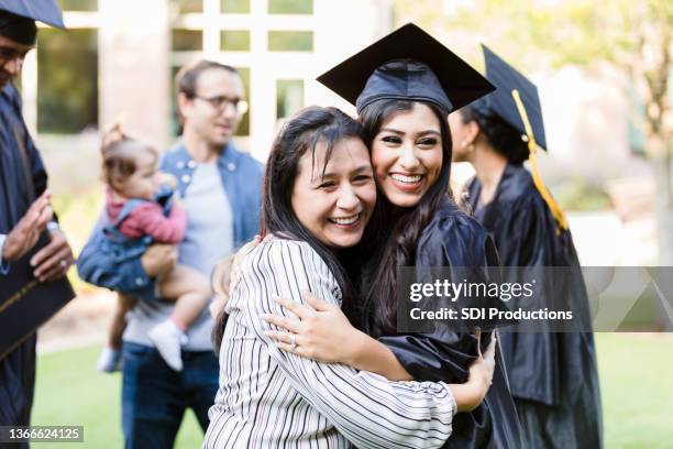 mutter und abschlusstochter posieren wange an wange für foto - graduierten talar stock-fotos und bilder