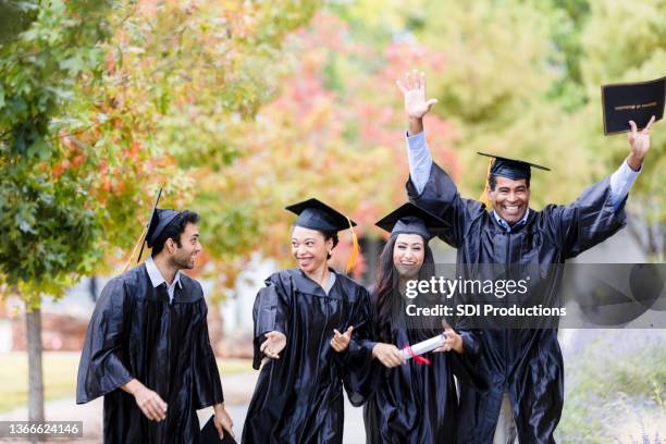 four graduating friends smile and talk as they walk together - animated graduation cap stock pictures, royalty-free photos & images