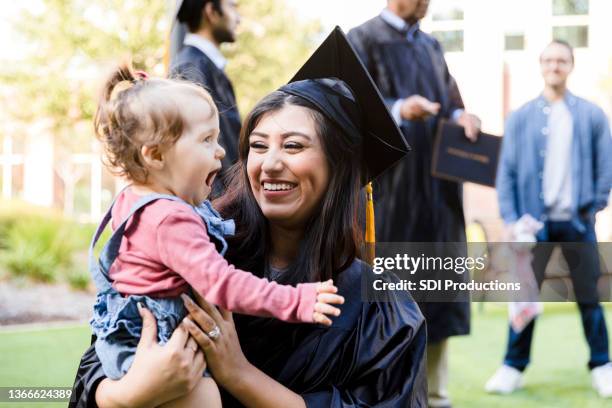 mother in cap and gown smiles at cute baby daughter - graduation excitement stock pictures, royalty-free photos & images