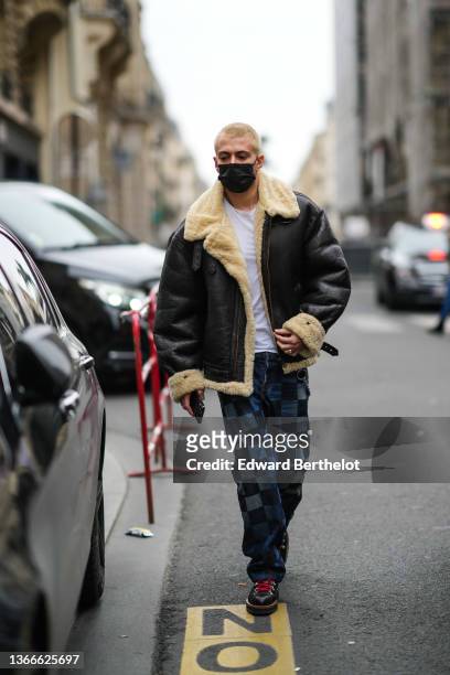 Guest wears a white t-shirt, silver rings, a black leather with pale yellow sheep interior oversized aviator coat, navy blue and blue checkered print...