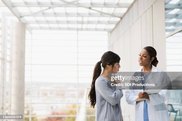 patient stops doctor in hospital walkway to discuss pain - speaking explaining young woman stock pictures, royalty-free photos & images