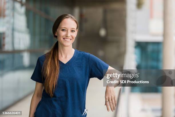 female surgeon leaning on balcony railing smiles for camera - real life science stock pictures, royalty-free photos & images