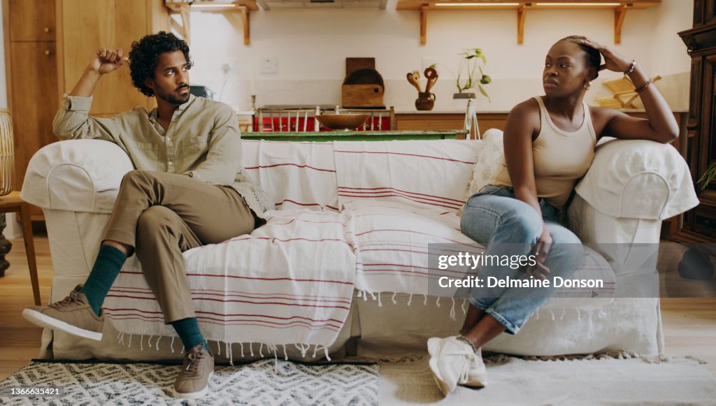 Full length shot of a young couple sitting on the sofa together and ignoring each other after an argument
