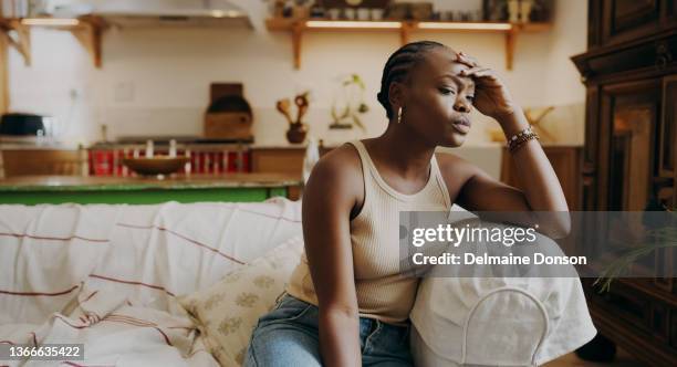 shot of an attractive young woman sitting alone on the sofa at home and feeling stressed - impatient stock pictures, royalty-free photos & images