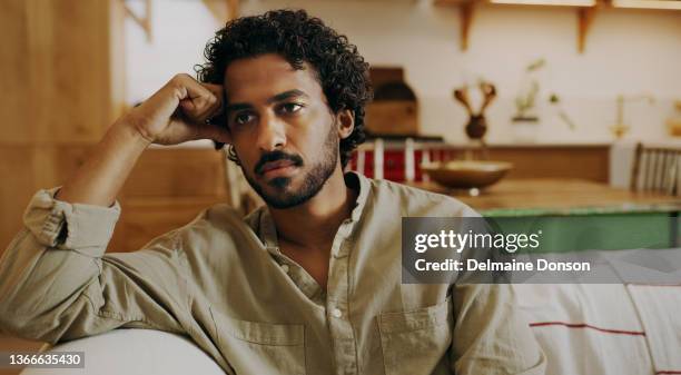 shot of a handsome young man sitting alone on the sofa at home and feeling stressed - impatient stock pictures, royalty-free photos & images