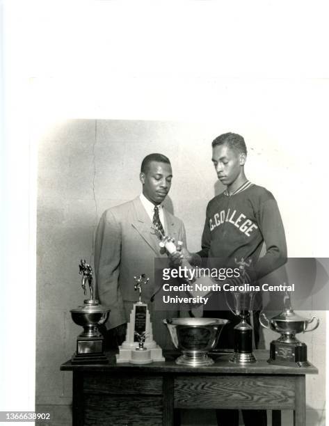 Olympian champion, Lee Calhoun and head track and field coach LeRoy Walker admire track and field trophy winnings. Lee Calhoun was a gold medalist in...