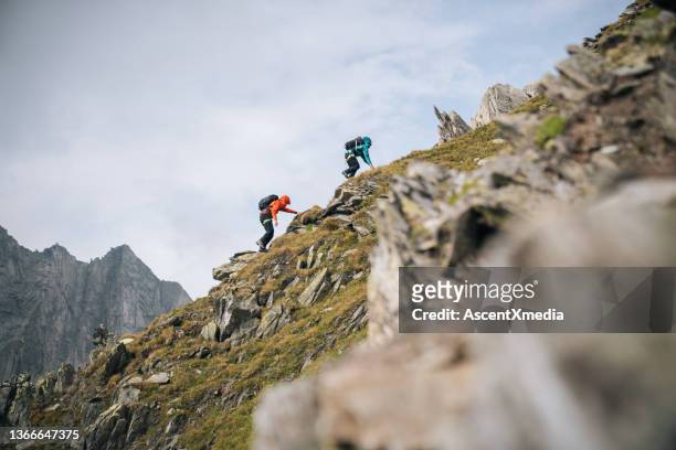 couple scramble up mountain ridge - team climbing up to mountain top stockfoto's en -beelden