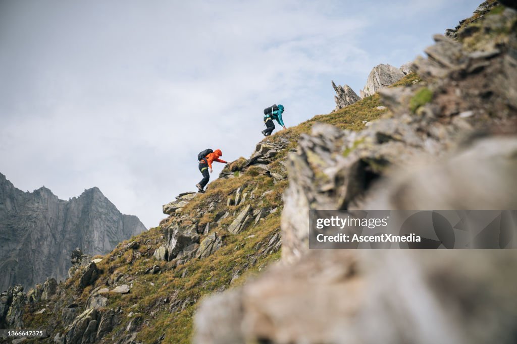 Couple scramble up mountain ridge