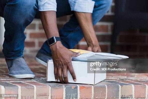 unrecognizable man squats to grab packages off front stoop - doorstep stockfoto's en -beelden
