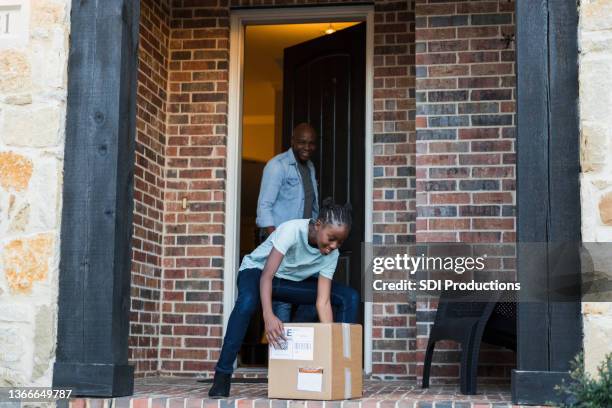 man watches daughter pick up surprise package - doorstep stock pictures, royalty-free photos & images