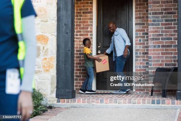 young boy carries package as father opens front door - doorstep stock pictures, royalty-free photos & images