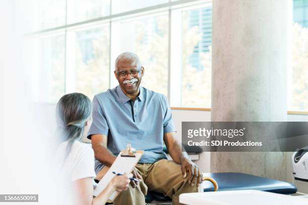 male physical therapy patient meets with physical therapist - man with clipboard imagens e fotografias de stock