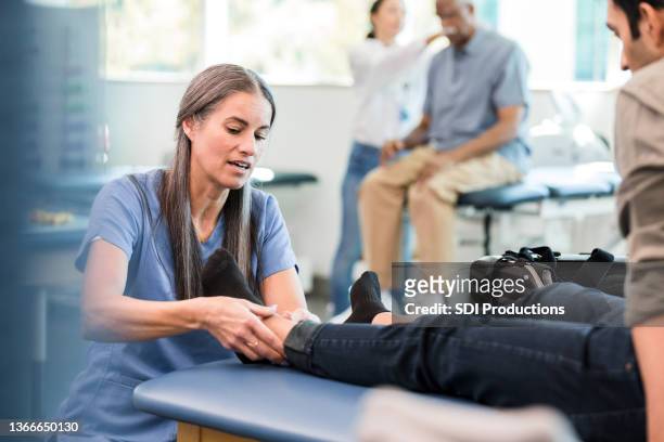 il fisioterapista lavora sulla caviglia dell'uomo durante la sessione di terapia fisica - man touching womans leg foto e immagini stock