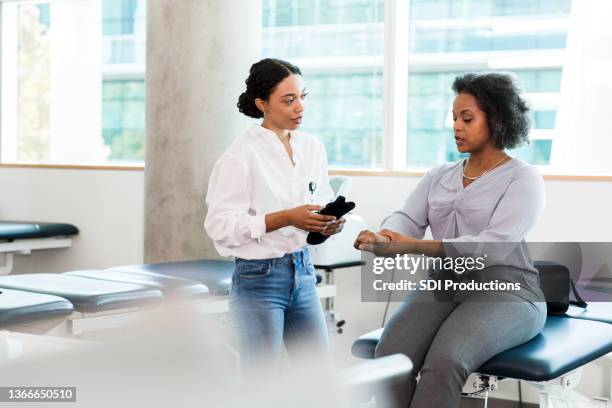 une femme d’affaires assise à une table d’examen discute de blessure avec un ergothérapeute - table dexamen médical photos et images de collection