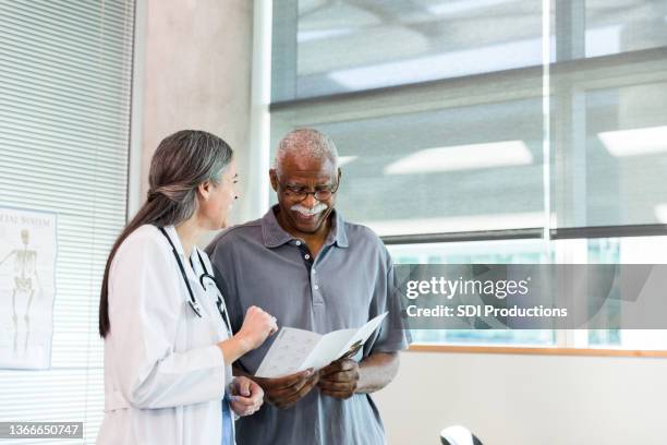 orthopedic doctor and senior patient smile while discussing brochure information - male doctor man patient stockfoto's en -beelden