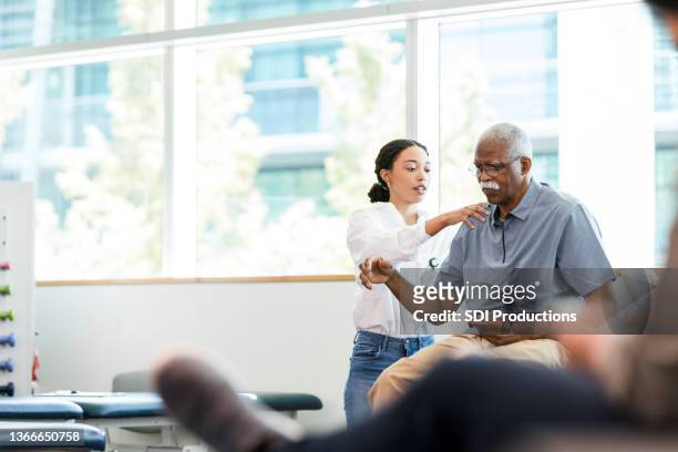 physical therapist examines senior man's shoulder - fysiotherapie stockfoto's en -beelden