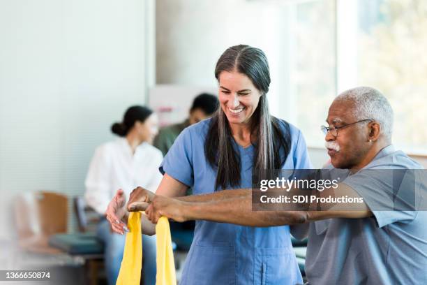 therapist smiles as senior man learns to use elastic band - arbetsterapi bildbanksfoton och bilder