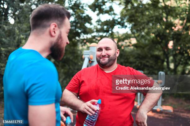 lächelnder übergewichtiger mann im gespräch mit fitnesstrainer nach dem training - chubby men stock-fotos und bilder