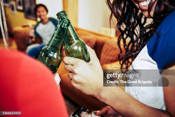 close up of female friends toasting with beer bottles at party - beer bottle cheers stock pictures, royalty-free photos & images