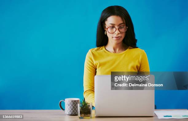 cropped shot of an attractive young woman working on her laptop at a desk in studio against a blue background - laptop studio shot stock pictures, royalty-free photos & images