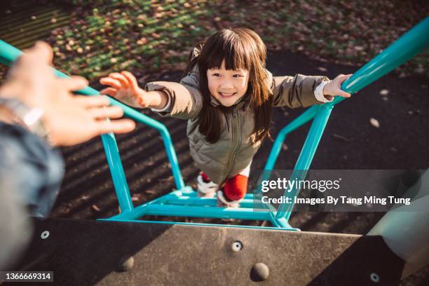 personal perspective of dad reaching out his hand helping her lovely little daughter climbing up the steps of a slide in play park - asian family in park stock-fotos und bilder