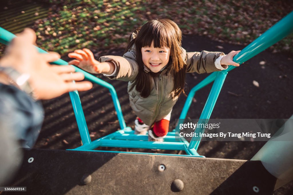 Personal perspective of dad reaching out his hand helping her lovely little daughter climbing up the steps of a slide in play park