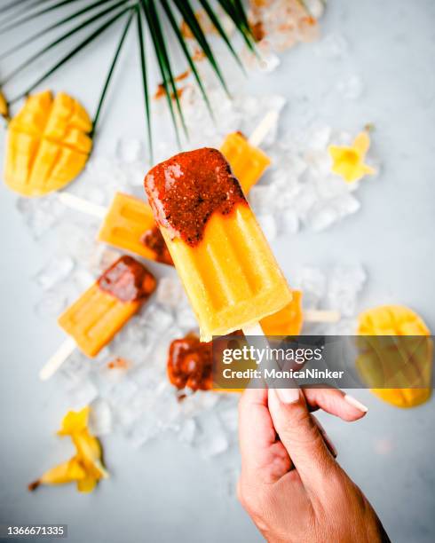 close up of hand holding  a mango popsicle - savory sauce stock pictures, royalty-free photos & images