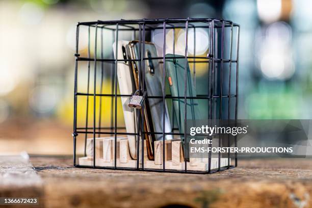 close up of three mobile phones locked in a cage for digital detox - verboten stock-fotos und bilder