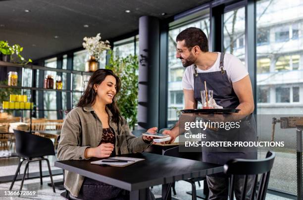 young and beautiful woman is paying with smartphone in a restaurant - kelner stockfoto's en -beelden