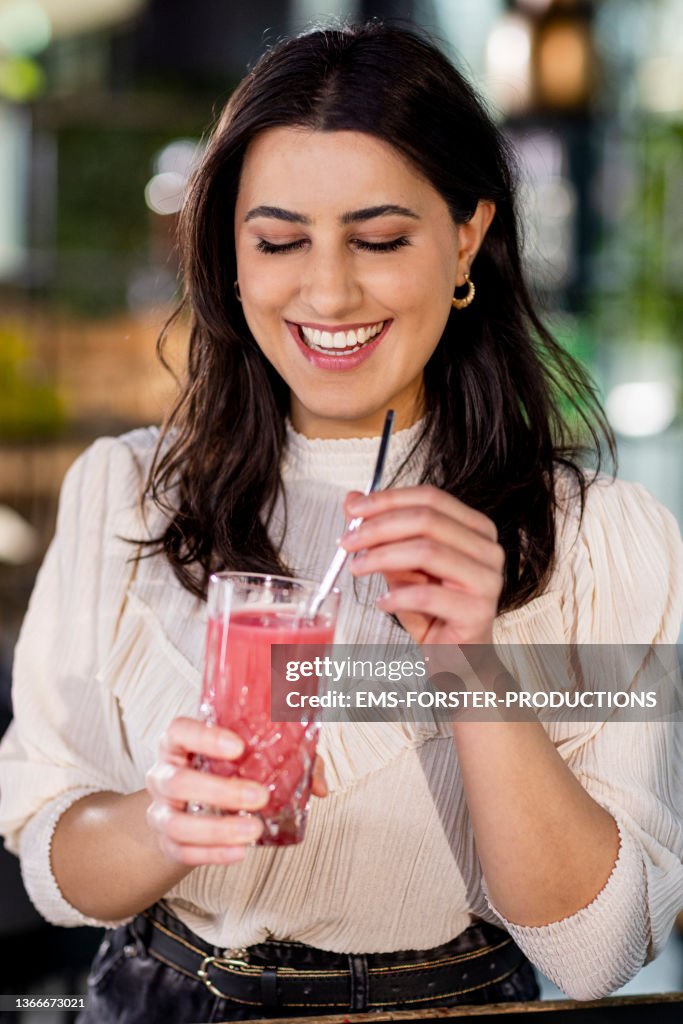 Smiling, young and beautiful woman is drinking fresh juice with a metal straw
