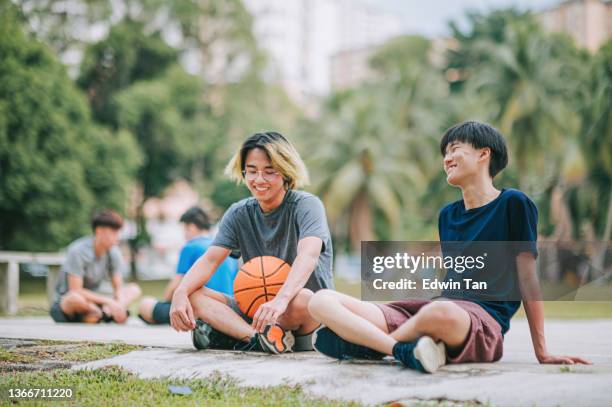 asian chinese teenage boy basketball player relaxing on basketball court with friends sitting on ground after game - chinese teenage boy stockfoto's en -beelden