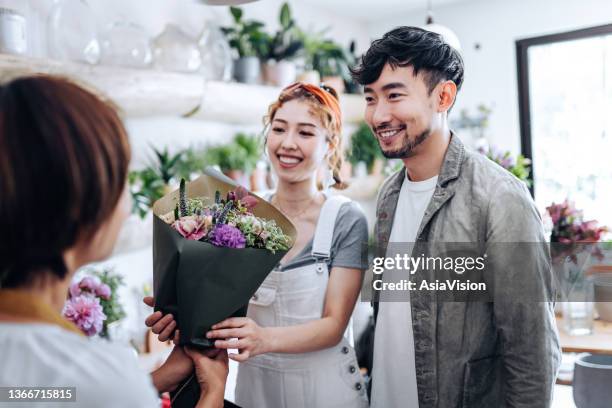 romantic young asian man buying flowers for his girlfriend in flower shop, smiling and chatting with the florist - flower shop stockfoto's en -beelden