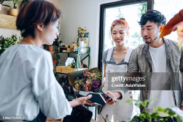 junges asiatisches paar, das blumen im blumenladen kauft. freund bezahlt den blumenstrauß mit seinem smartphone, scannt und bezahlt eine rechnung an einem kartenautomaten, der schnell und einfach kontaktlos bezahlt. nfc-technologie, tap-and-go-konzept - nfc payment stock-fotos und bilder