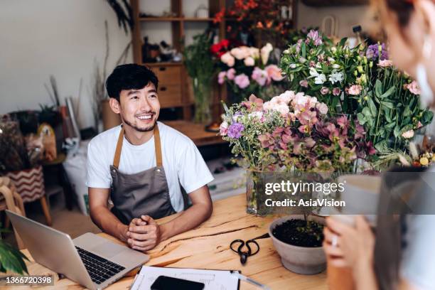 jeune couple asiatique, propriétaire d’un petit magasin de fleurs, utilisant un ordinateur portable et travaillant ensemble dans le magasin contre les fleurs et les plantes. discuter de questions commerciales. démarrage d’entreprise, partenariat d’ - self employed photos et images de collection