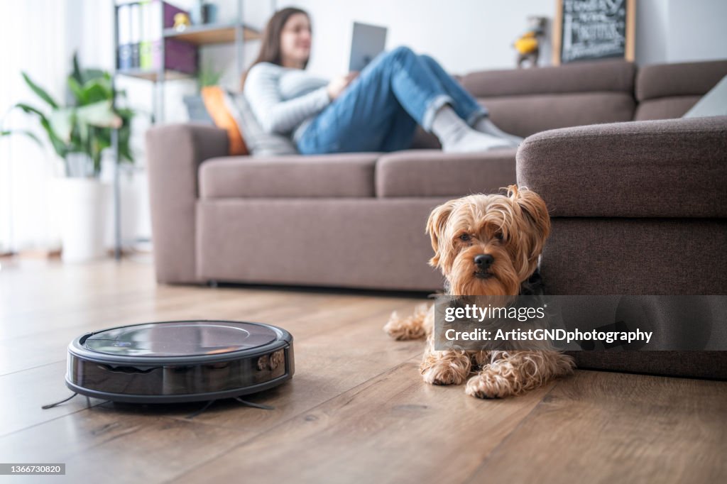 Frau und Hund entspannen sich im Wohnzimmer, während der Roboter staubt.