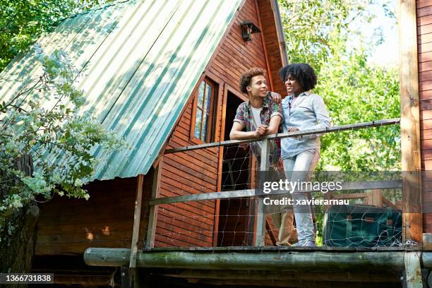 couple standing outside cabin at start of weekend getaway - vakantiehuis stockfoto's en -beelden