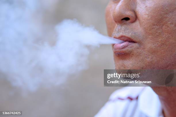 a closeup of a man breathing out the cigarettes' smoke - nikotin stock-fotos und bilder