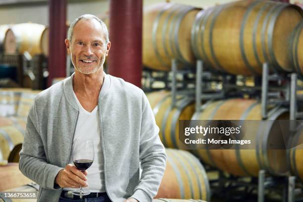 portrait of smiling man with red wine in cellar - gray jacket fotografías e imágenes de stock