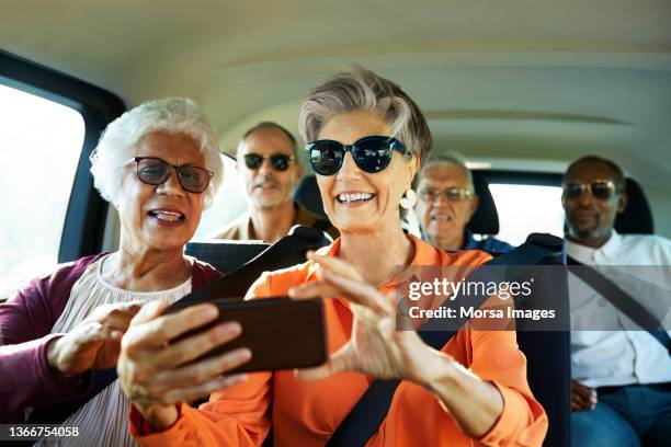 smiling woman using smart phone by friend in car - retirement stock photos et images de collection