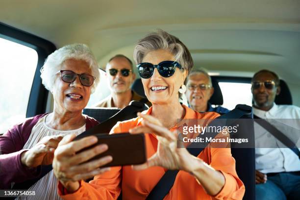smiling woman using smart phone by friend in car - couple in car smiling stockfoto's en -beelden