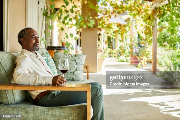 smiling man with wine glass looking away at porch - south africa wine stock pictures, royalty-free photos & images