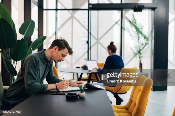 business people work during a coffee break, in their office. a woman uses a laptop while a man sorts documents. - cool office stockfoto's en -beelden