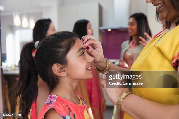 indian mother placing bindi on forehead of smiling daughter - indian art culture and entertainment ストックフォトと画像