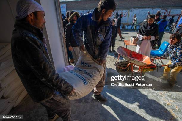 Workers hoist a sack of flour as Afghans collect a monthly ration of staple food - flour, lentils, oil and salt - to stave off impending famine from...