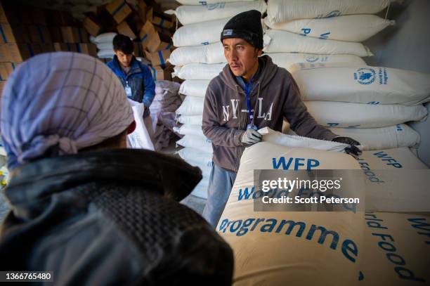 Workers hoist sacks of flour as Afghans collect a monthly ration of staple food - flour, lentils, oil and salt - to stave off impending famine from a...