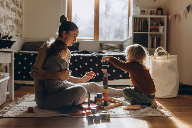 young mother playing with children while sitting on floor at home with wooden toys - kids stock pictures, royalty-free photos & images