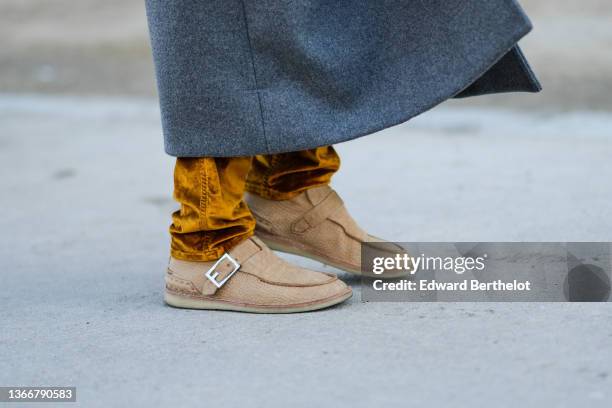 Guest wears a gray long coat, a yellow mustard / brown shiny velvet large pants, brown suede crocodile print pattern shoes, outside Schiaparelli...