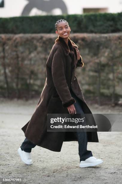 Model wears a black pullover, a brown suede with fur interior oversized long coat, black denim flared jeans pants, white leather sneakers from...