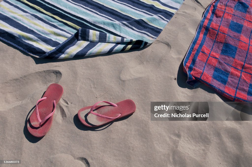 Towels and slip on thongs resting on sand